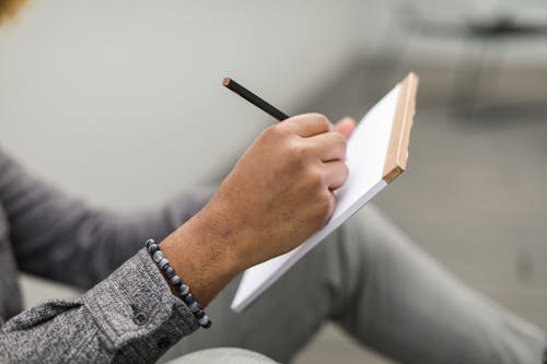 Person in Gray Long Sleeves Writing on a Notebook