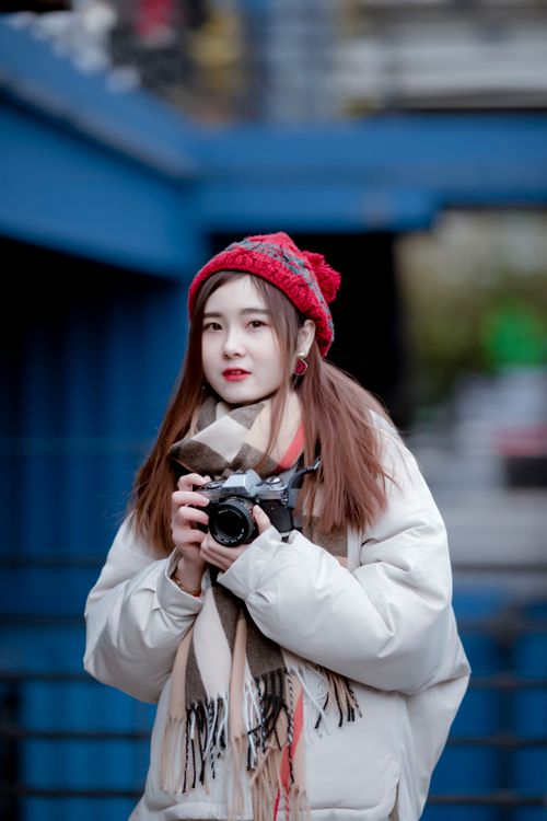 Free Portrait of an Asian woman holding a camera in an urban winter setting, showcasing her confident and stylish presence. Stock Photo