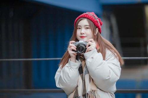 Free A young woman in winter attire holding a camera, outdoors in an urban area. Stock Photo