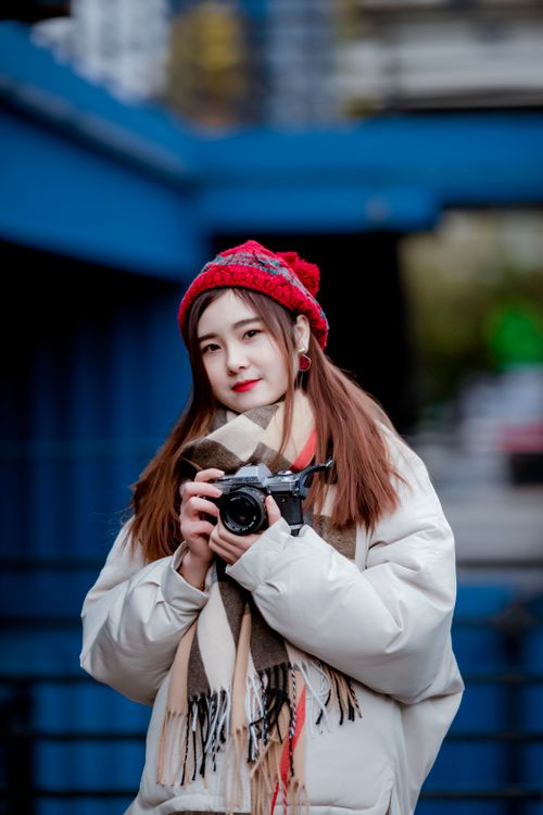Free A young woman in winter clothes holding a camera outdoors, ready to capture moments. Stock Photo