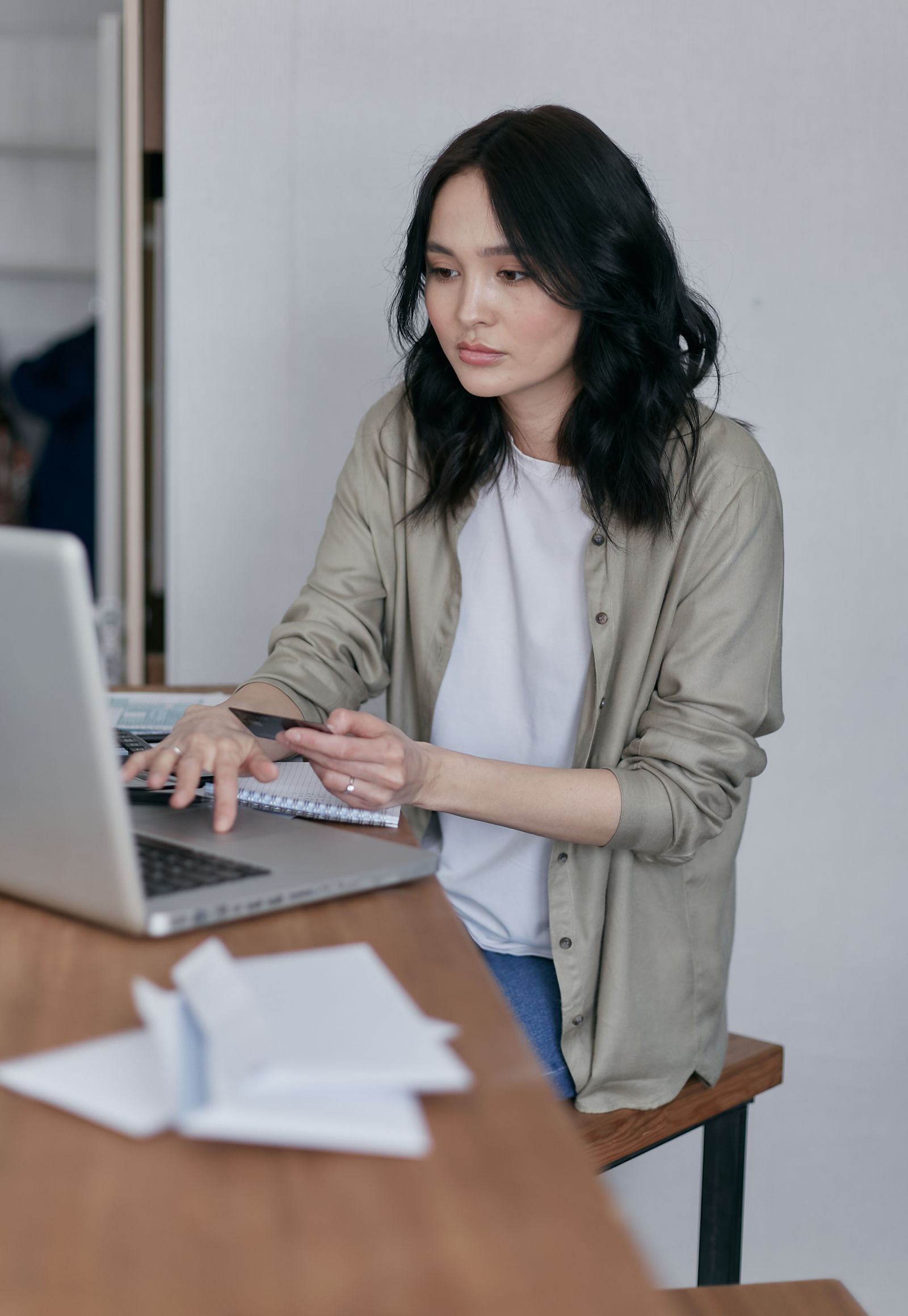 Asian woman using a laptop with bills and financial documents while managing personal finances
