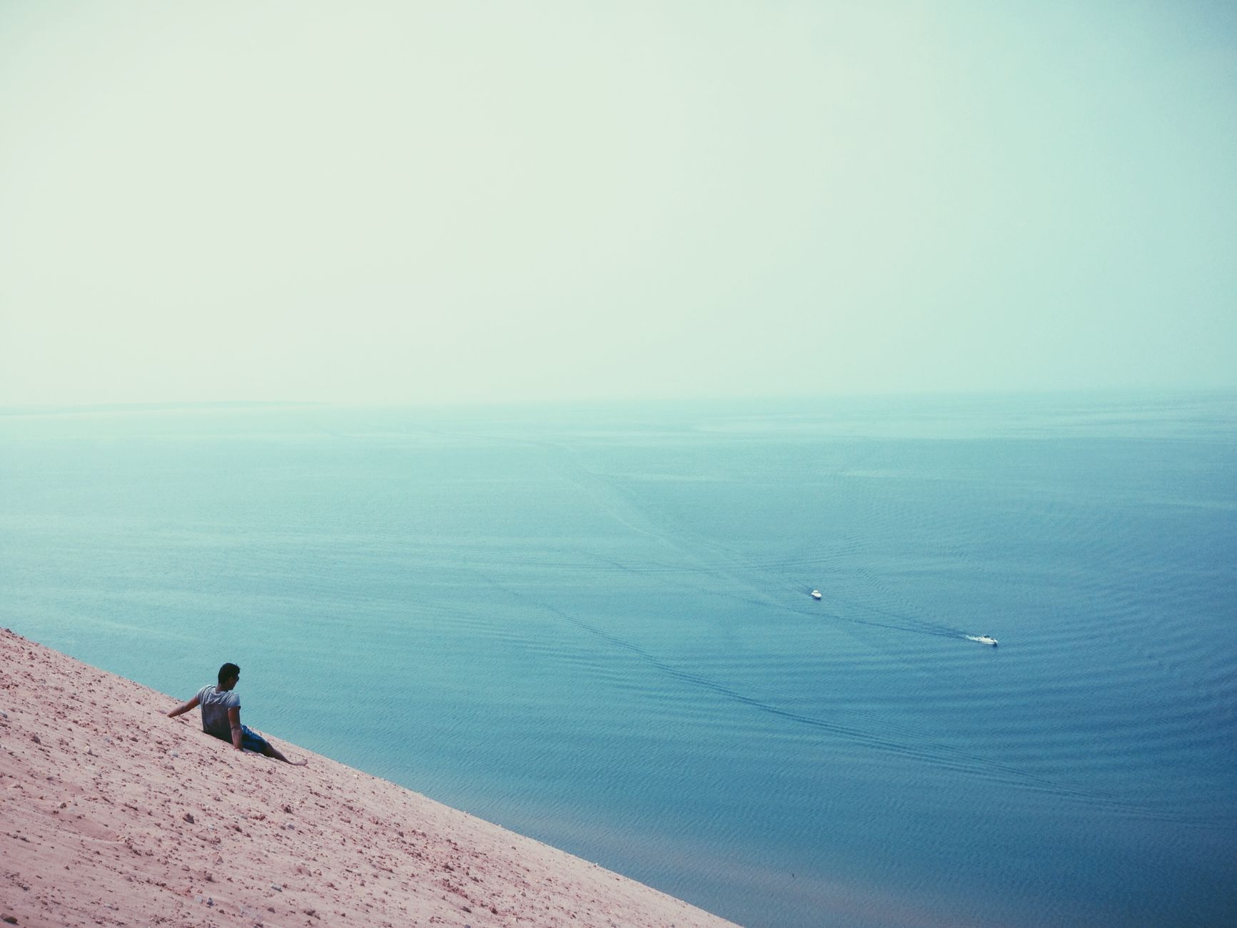 a traveler in a windbreaker studying a paper map at a Lake Michigan overlook with dunes and blue wat