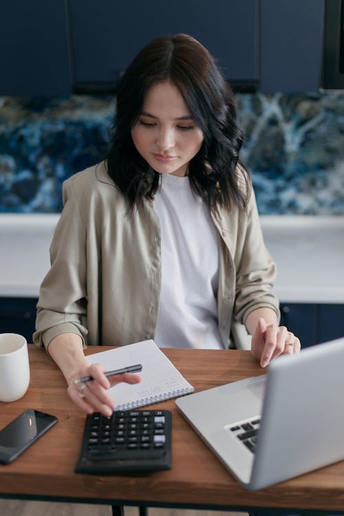 Free Woman Using a Calculator While Sitting In Front of a Laptop Stock Photo
