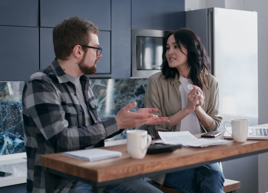Una pareja joven teniendo una conversación seria sobre finanzas en su cocina.