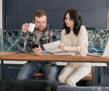 A Man Looking at the Paper while Holding a Coffee and Phone
