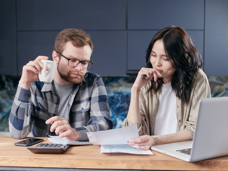 Coworkers At Table With Documents And Calculator Near Laptop