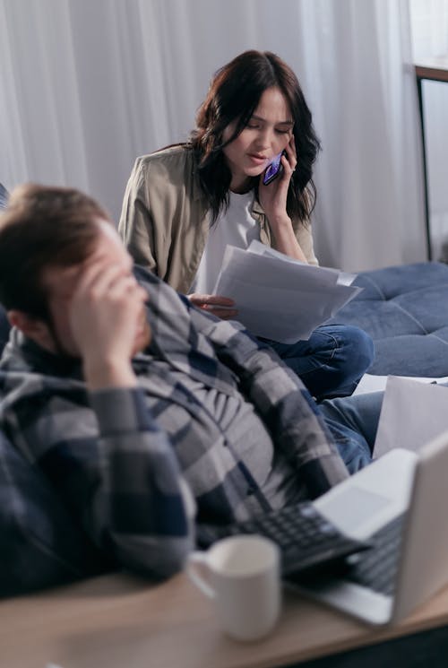 Free Woman on the Phone Holding Paperwork Beside a Man in Deep Thoughts Stock Photo
