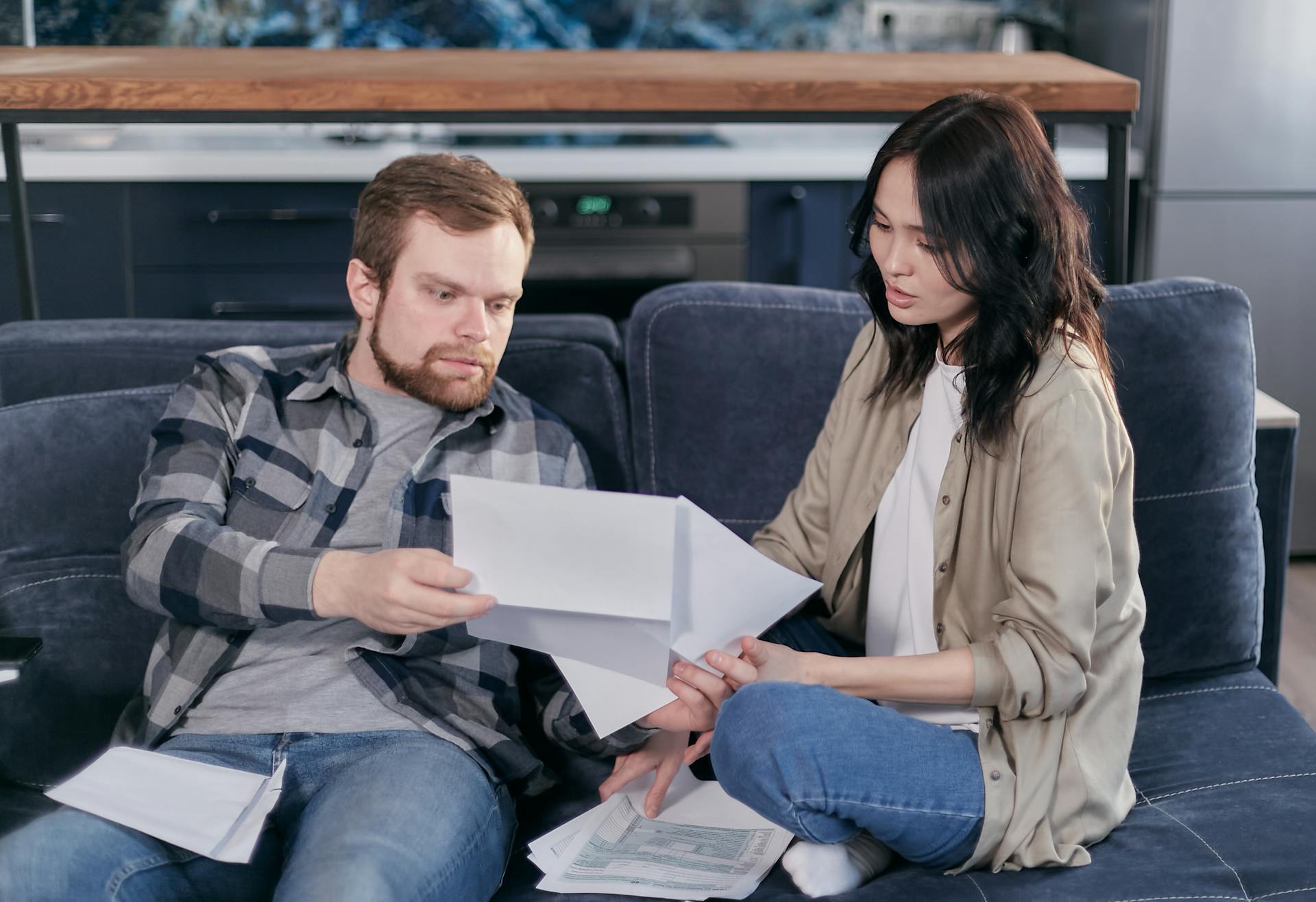 Asian woman and Caucasian man discussing taxes on couch.