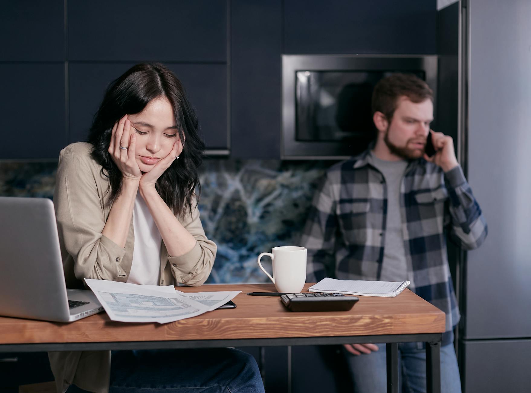 A couple dealing with financial stress, surrounded by bills and a laptop indoors.
