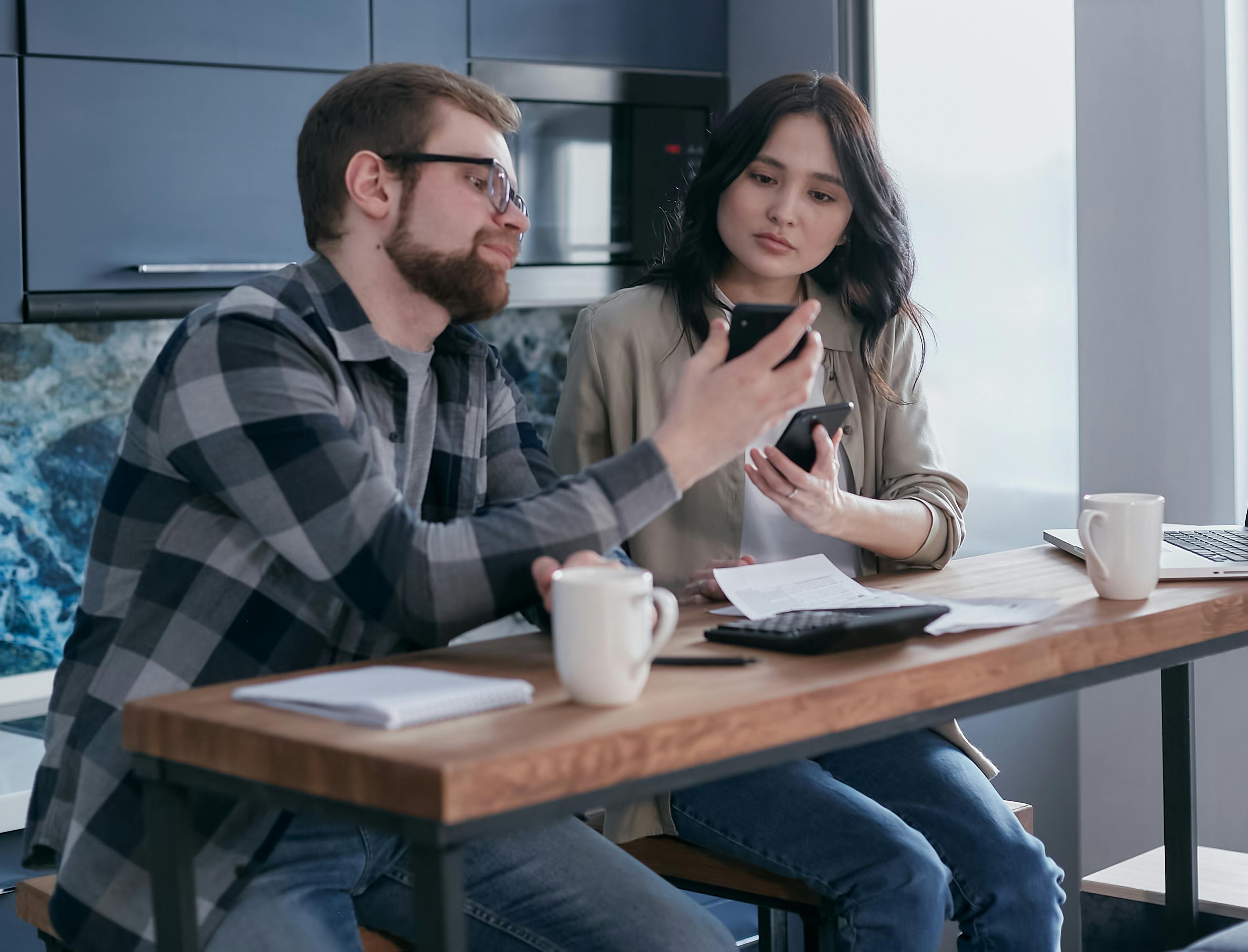 a couple sitting near the wooden table while holding mobile phones