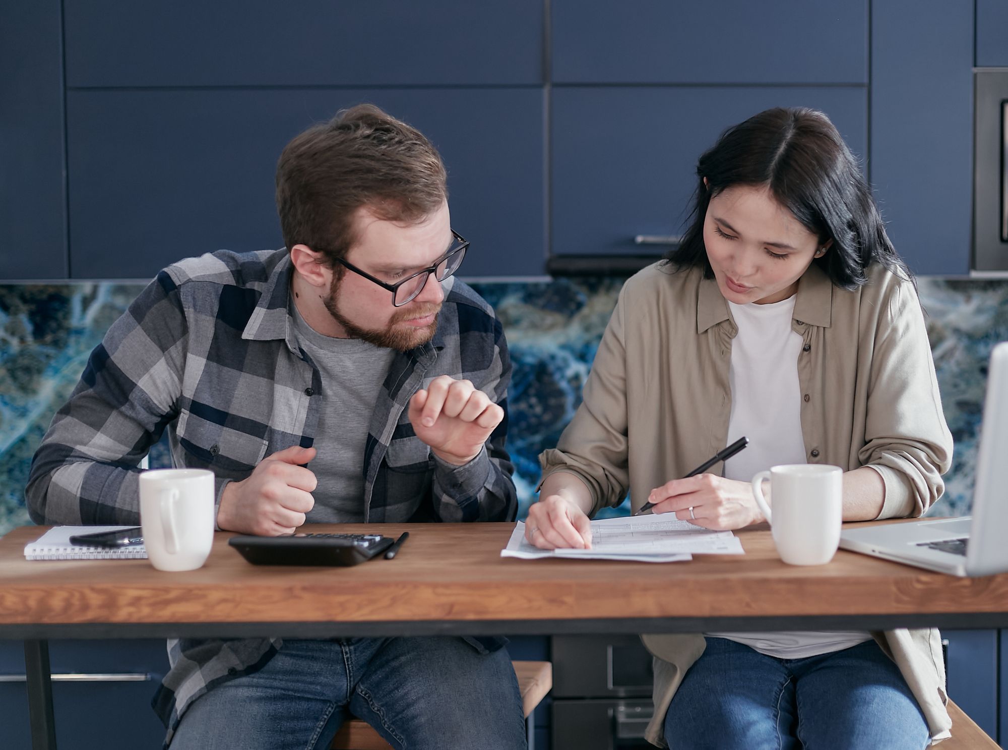 Couple reviewing bills and a calculator together at their kitchen table