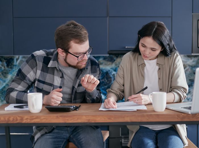 A couple sitting at a wooden table reviewing documents and discussing finances