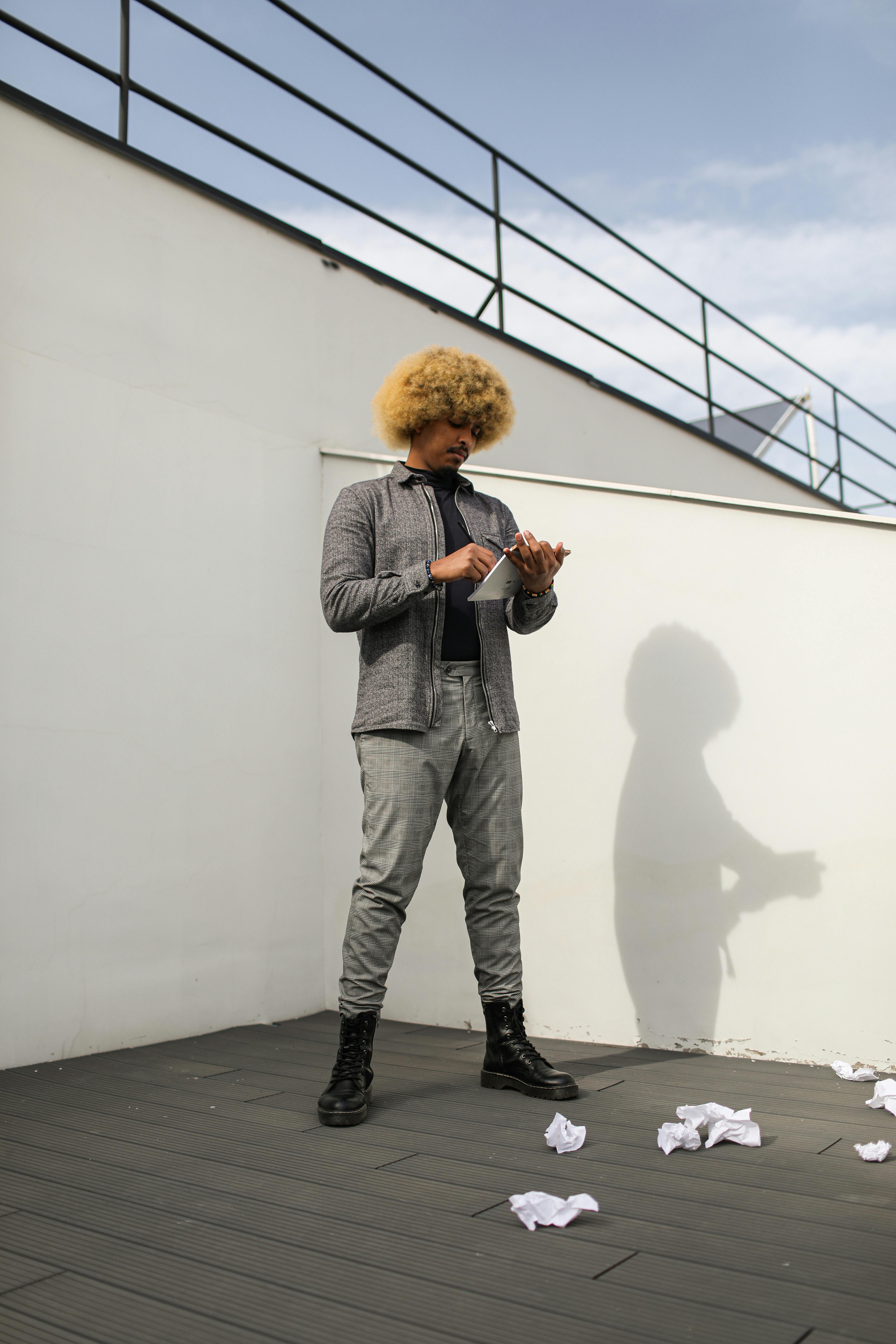Modern fashion photo of a man with Afro hair holding a tablet on a terrace.