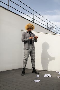Modern fashion photo of a man with Afro hair holding a tablet on a terrace.