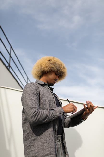 A Low Angle Shot of a Man Writing on Notebook