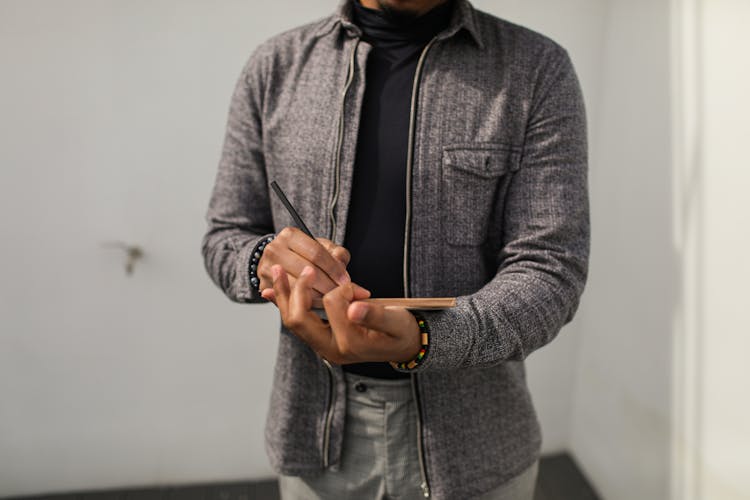 A Person In Gray Jacket Writing On Notebook