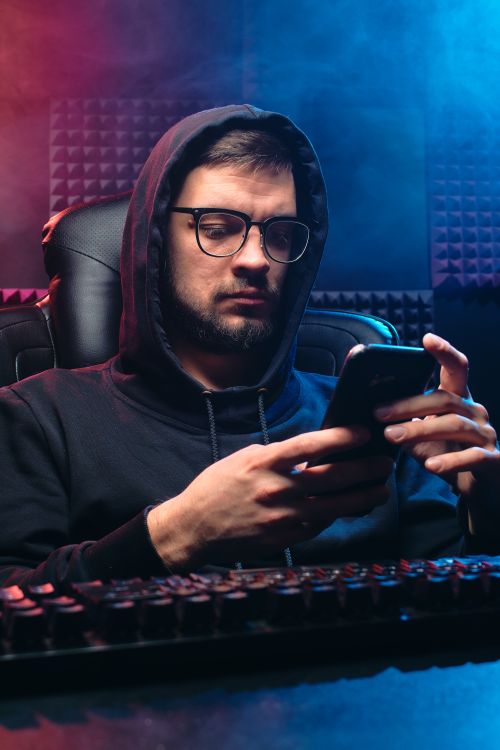 Free Man in hoodie using smartphone, representing cybersecurity themes like hacking and privacy. Stock Photo