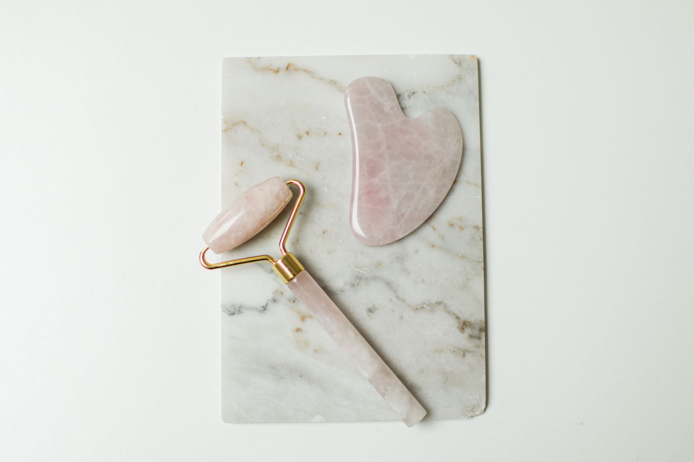Rose quartz facial roller and gua sha tool arranged on marble