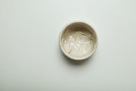 Top view of a ceramic bowl with facial cream over a minimalist gray backdrop.