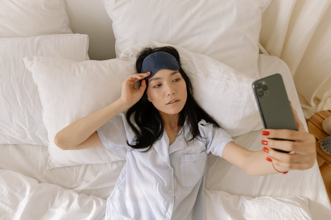 Free Woman in Pajamas Lying on Bed Taking Selfie Stock Photo