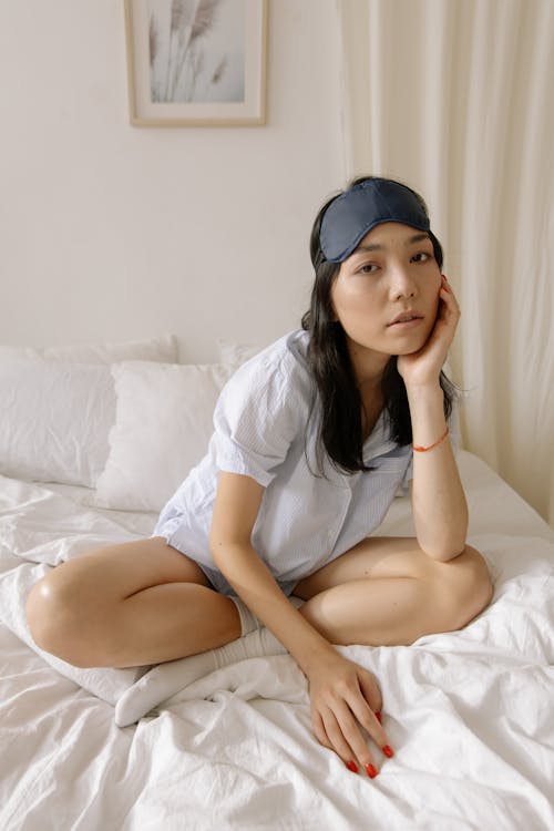 Woman in Sleepwear with Eye Mask Sitting on Bed 