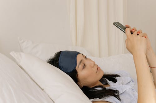 Free Young Woman Lying in Bed and Using a Phone  Stock Photo