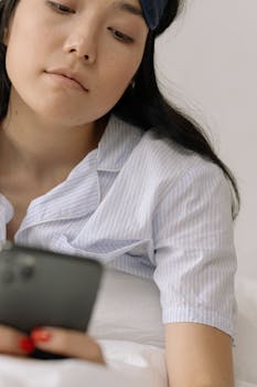 Young woman in pajamas using phone in bed, relaxed and tranquil morning.