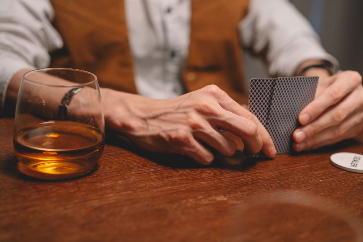 Casinoprom bahis kültürünü yansıtan, masada oturan ve düşünceli bir ifadeyle kart inceleyen kişi