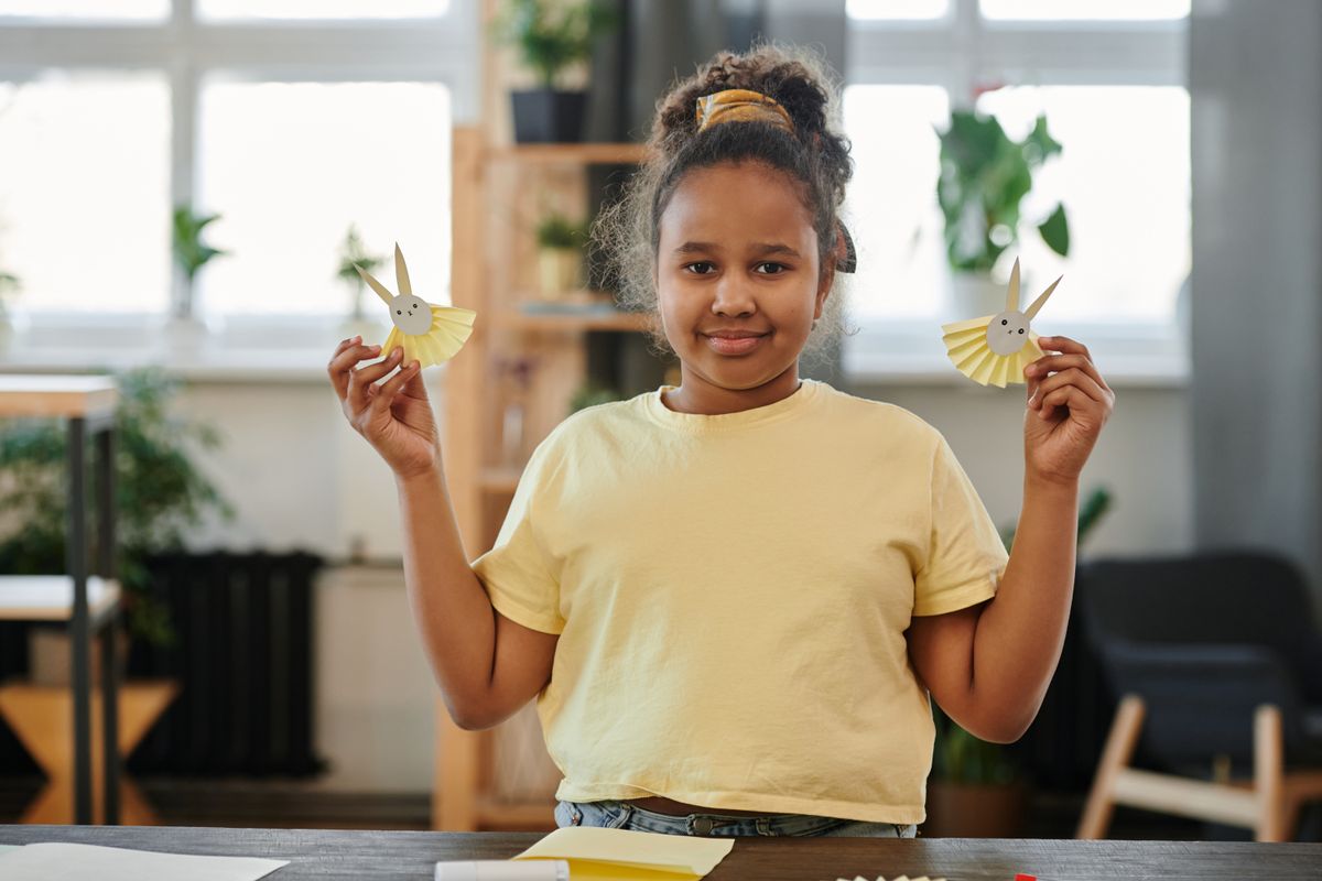 A young girl presenting her paper crafts, including a paper plate horse mask