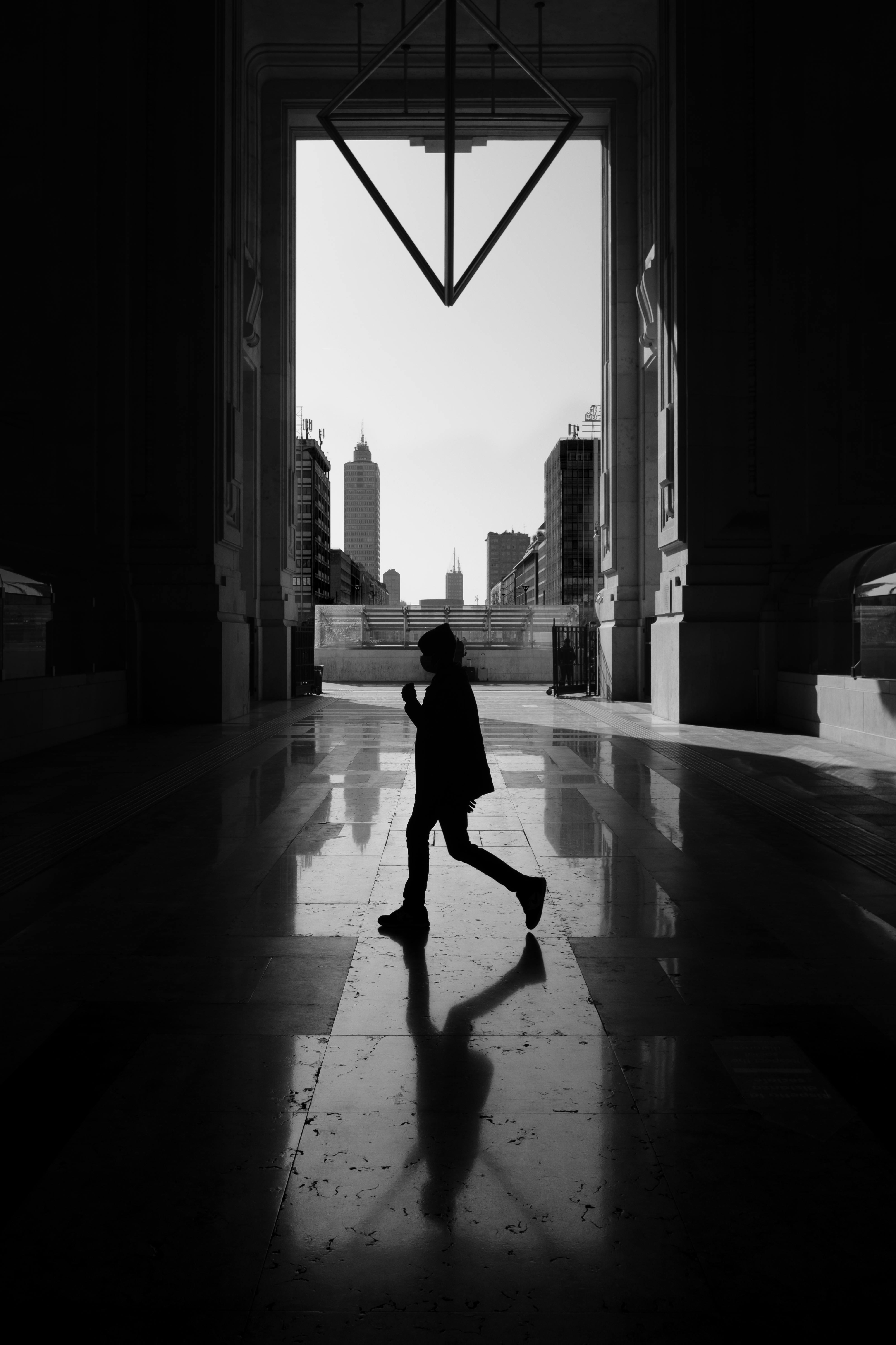 grayscale photo of woman walking on sidewalk