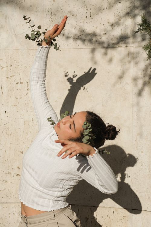 Free A woman in a white shirt strikes a pose with eucalyptus shadows on a sunny day. Stock Photo