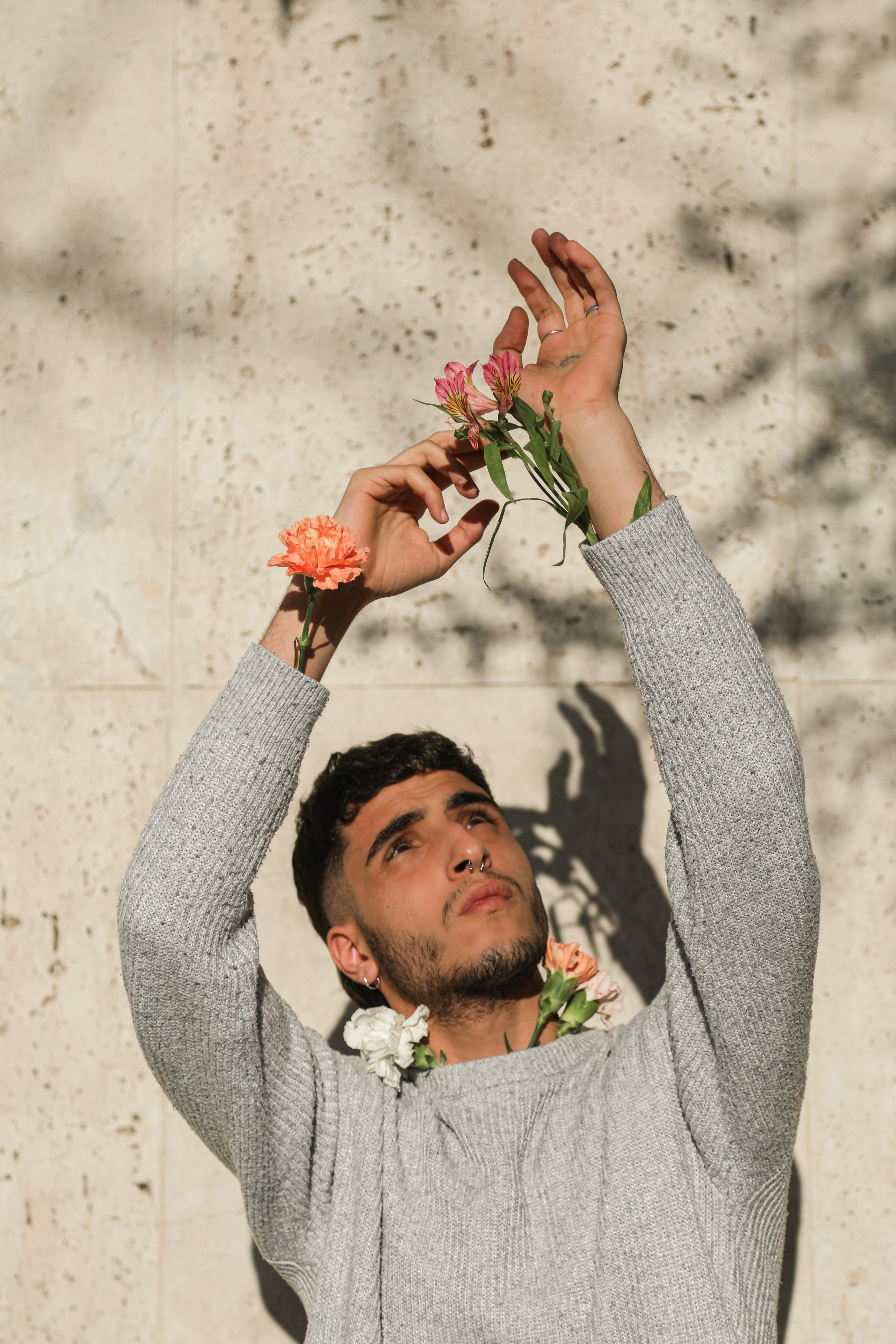 A man poses with flowers in a sweater, casting shadows on a sunny day.