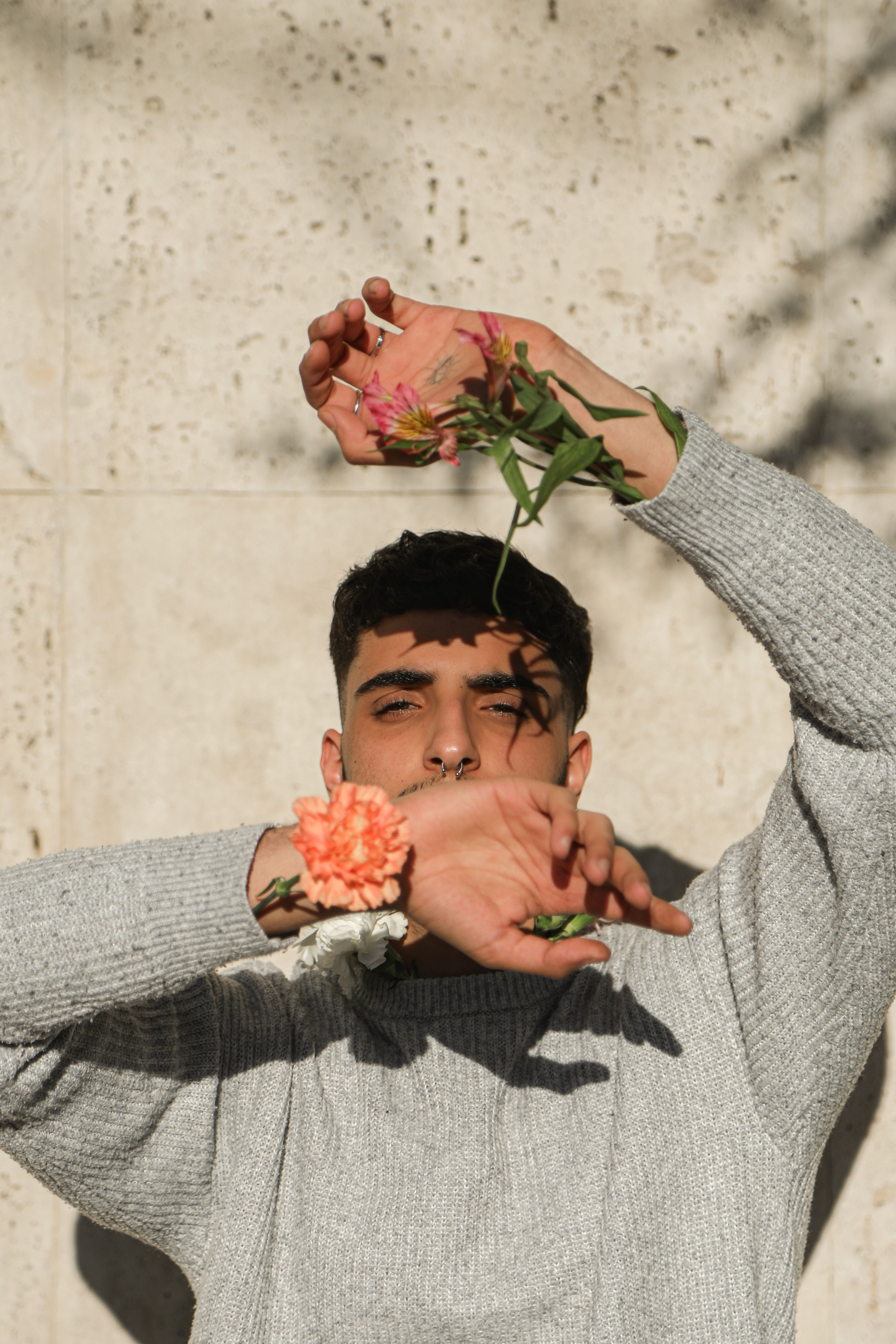 Young man in a sweater poses creatively with flowers in natural sunlight.