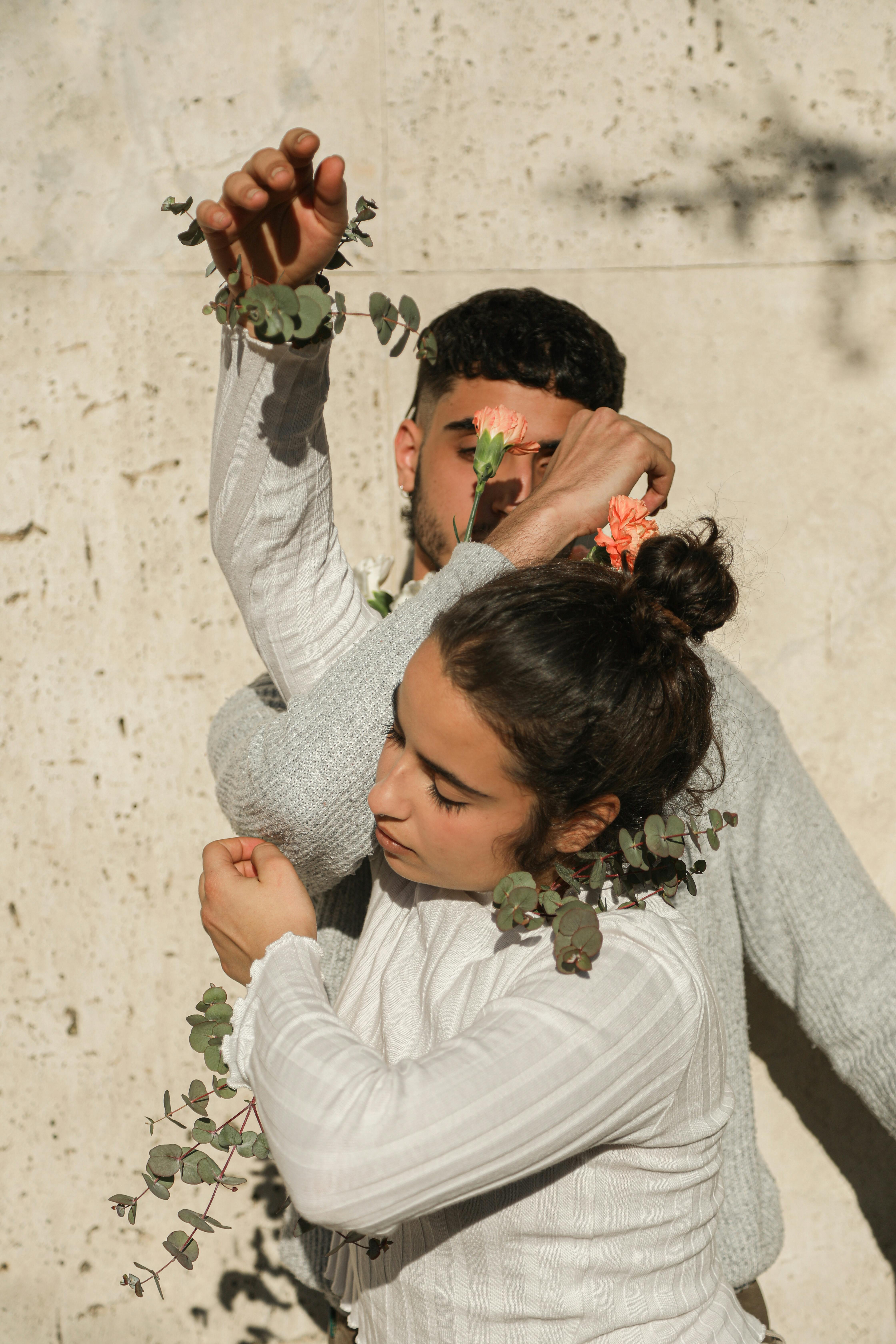 Contemporary portrait of a couple in stylish attire adorned with floral accents, set against a neutral backdrop.