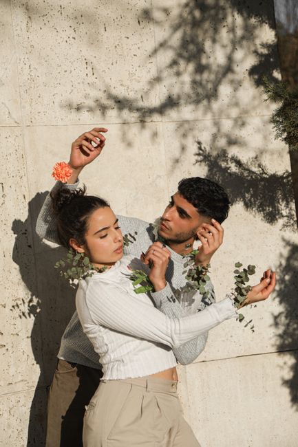 A couple poses with floral accents against a textured wall, capturing intimacy and nature.