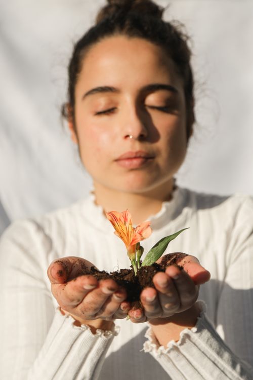 Free A serene woman holding a small flower in soil, embodying calmness and connection to nature. Stock Photo
