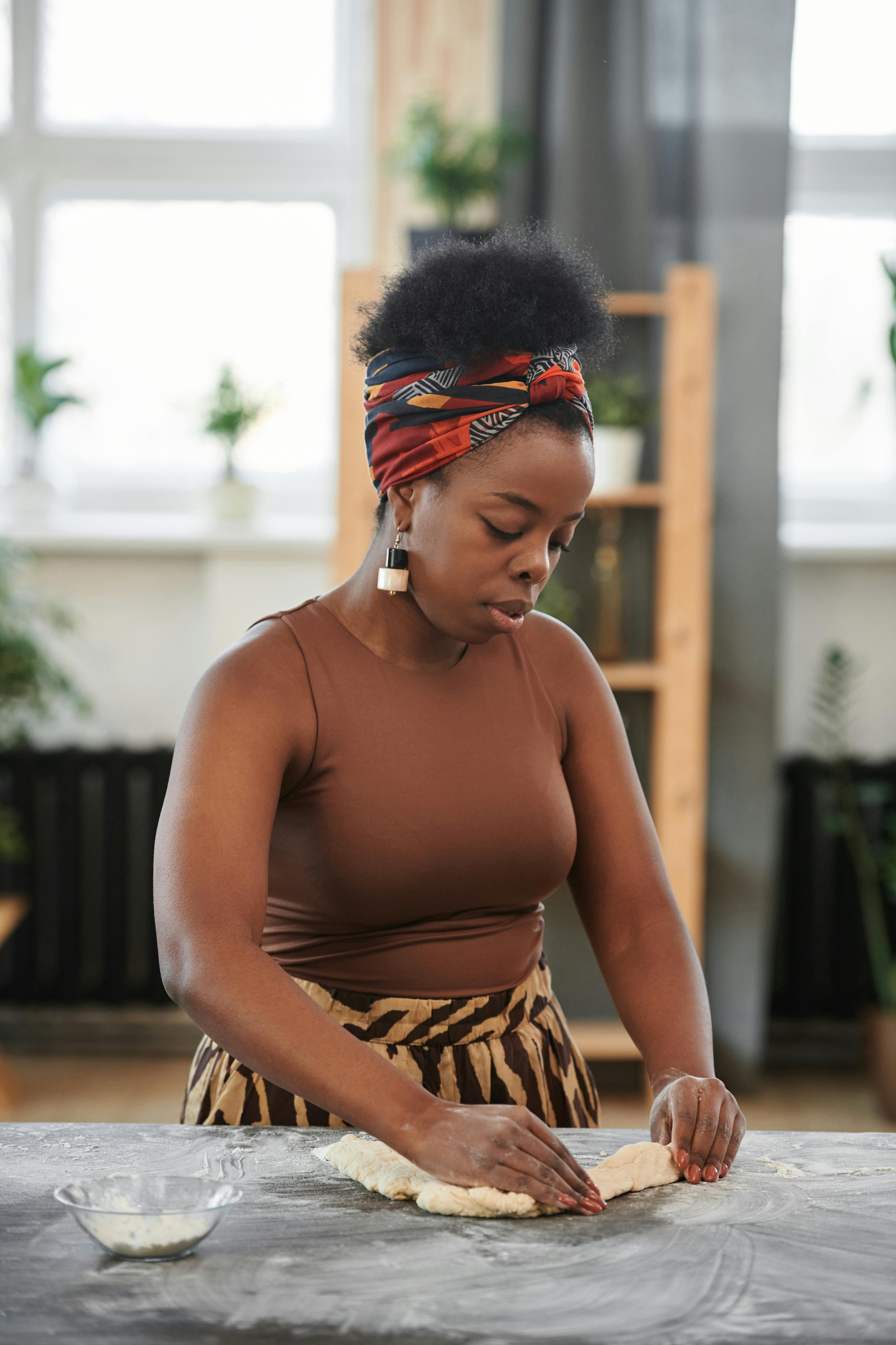 A young woman skillfully kneads dough in a cozy indoor kitchen setting, showcasing baking in a warm atmosphere.