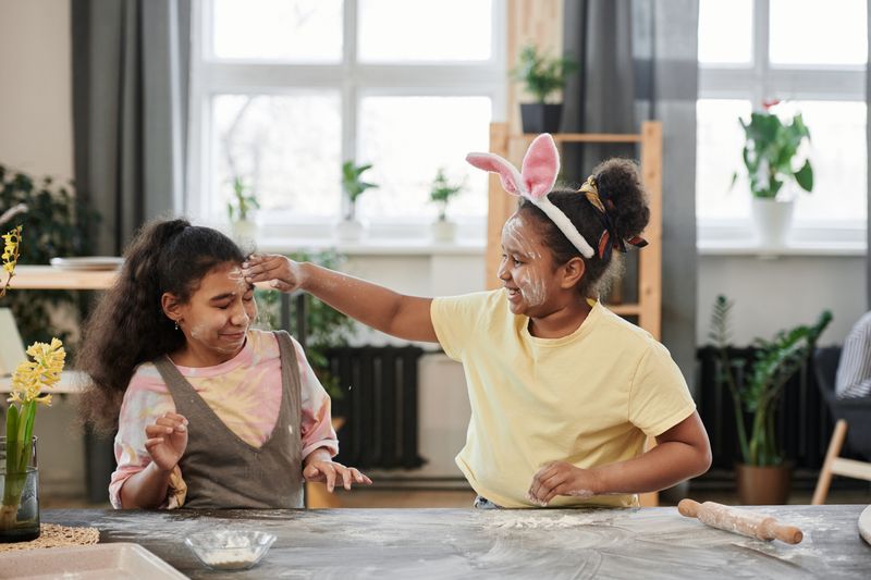 Two girls enjoy playful cooking with flour and laughter in a cozy kitchen setting.