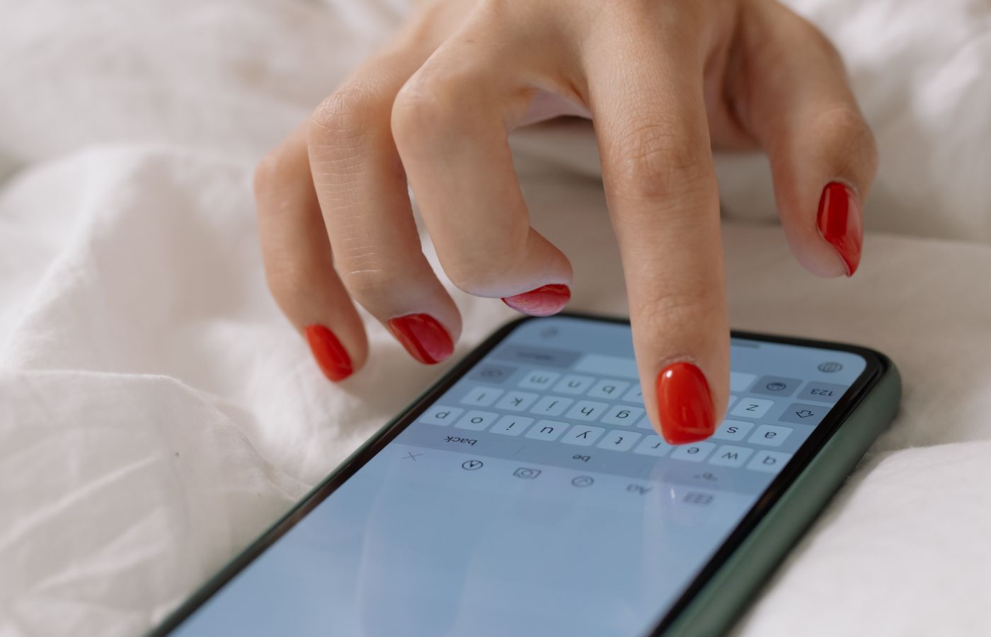 A close-up view of a woman's manicured hand typing on a smartphone, indoors.