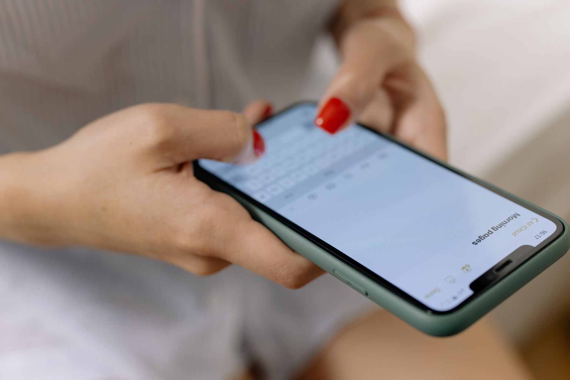 Close-up of a woman with red nails typing on a smartphone indoors, focusing on hands.