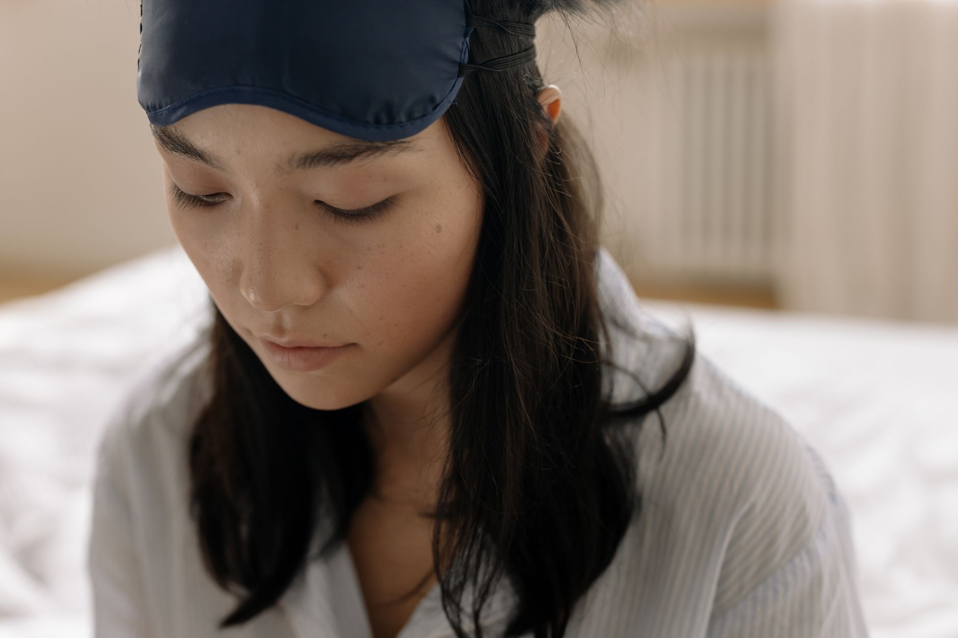 A serene young woman wearing a sleep mask and striped shirt, relaxing indoors.