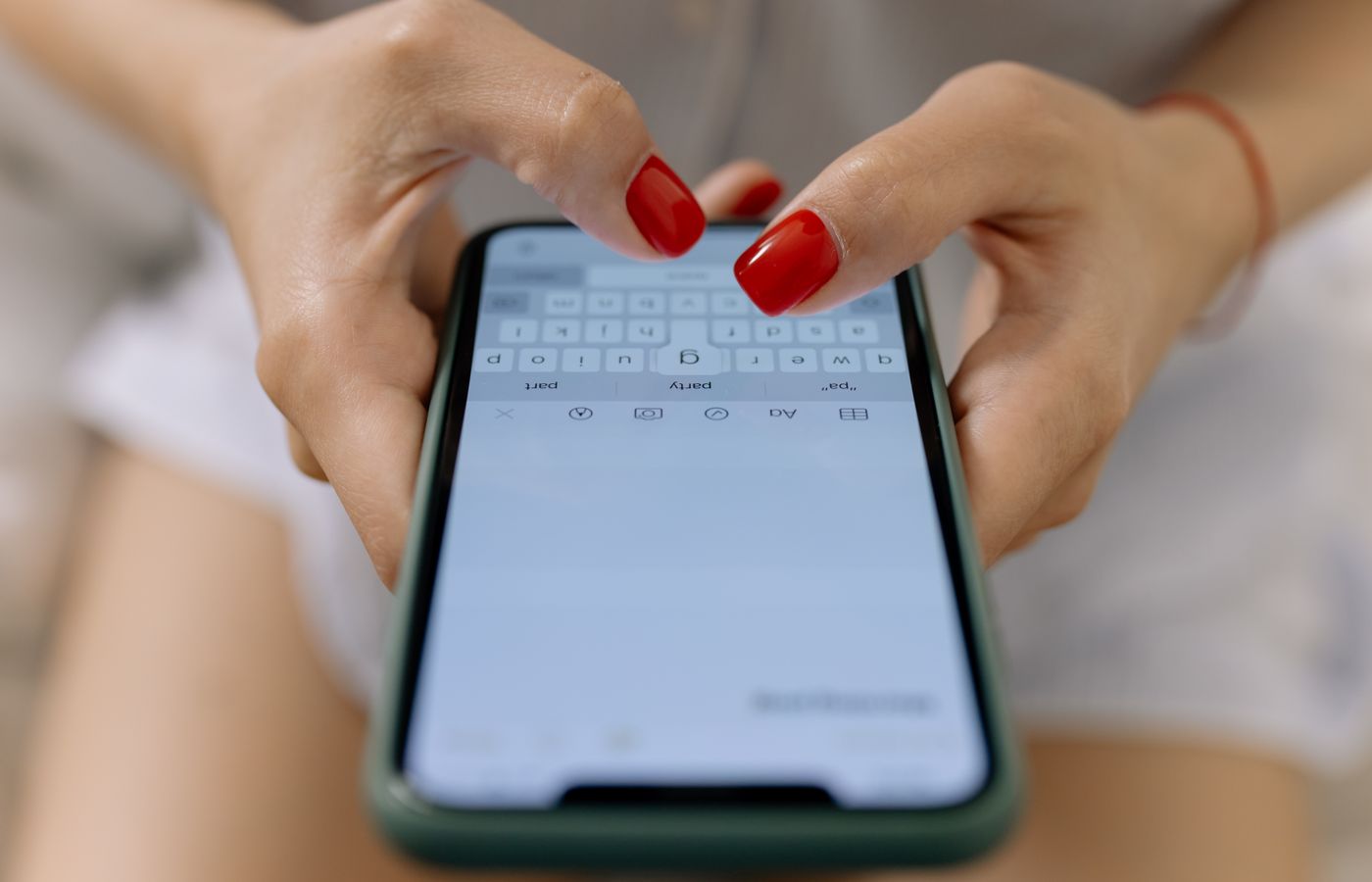 Close-up image of hands with red nails typing on a smartphone screen, showcasing modern technology.