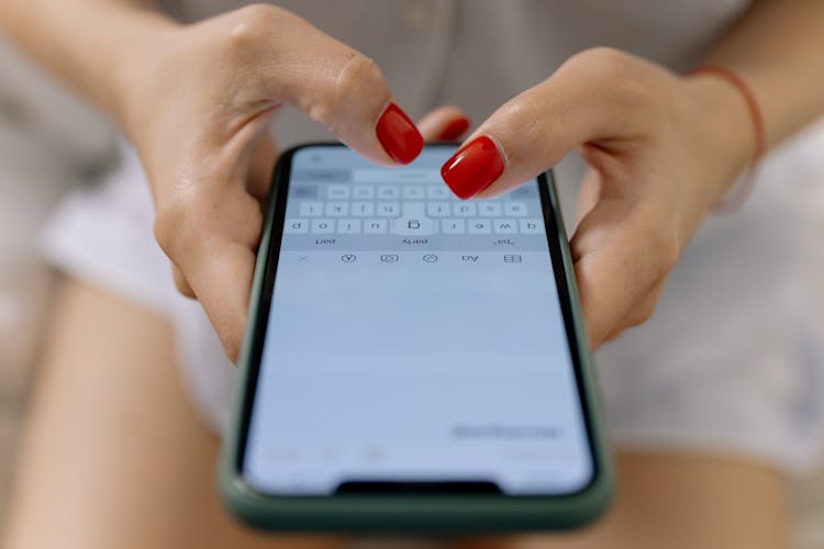 Hands Of A Woman With Red Nails Typing On A Smartphone