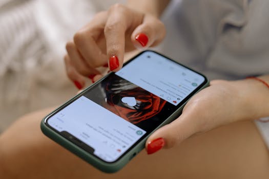 Close-up of a woman with red nails using a smartphone indoors, showcasing social media browsing.