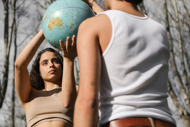 A Woman In Brown Crop Top And A Person In White Tank Top Holding A Globe