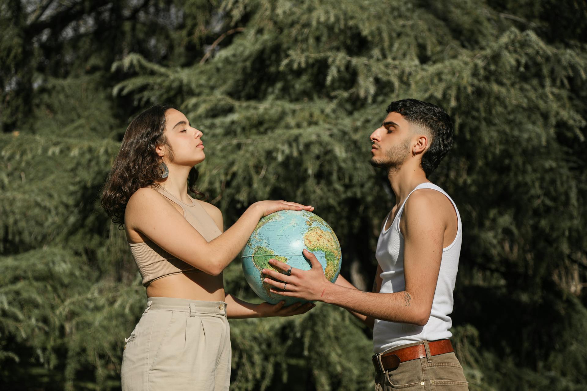 A young couple holds a globe outdoors, symbolizing unity and cooperation.