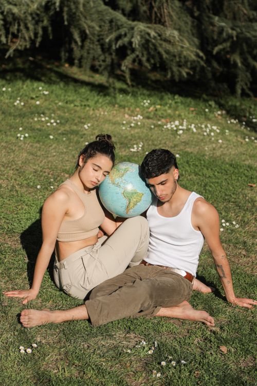 Free Young couple sitting on grass with globe representing connection to earth and nature. Stock Photo