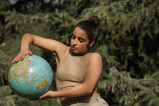 Focused young woman holding a globe outdoors against a backdrop of green trees.