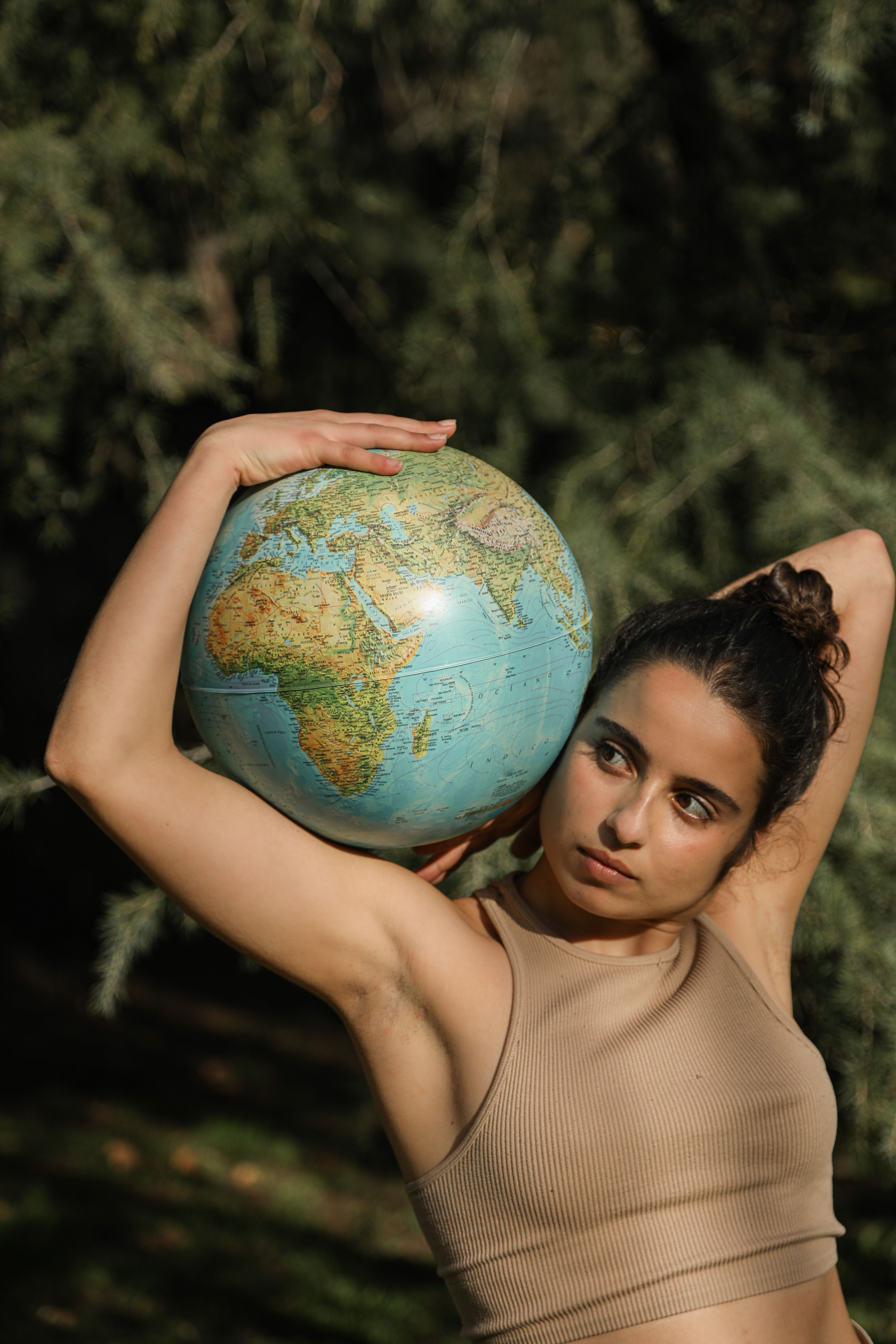 A woman poses outdoors with an earth globe, symbolizing global awareness and connection.