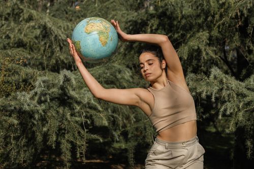 Free A woman gracefully poses with a globe amidst lush greenery, symbolizing environmental awareness. Stock Photo